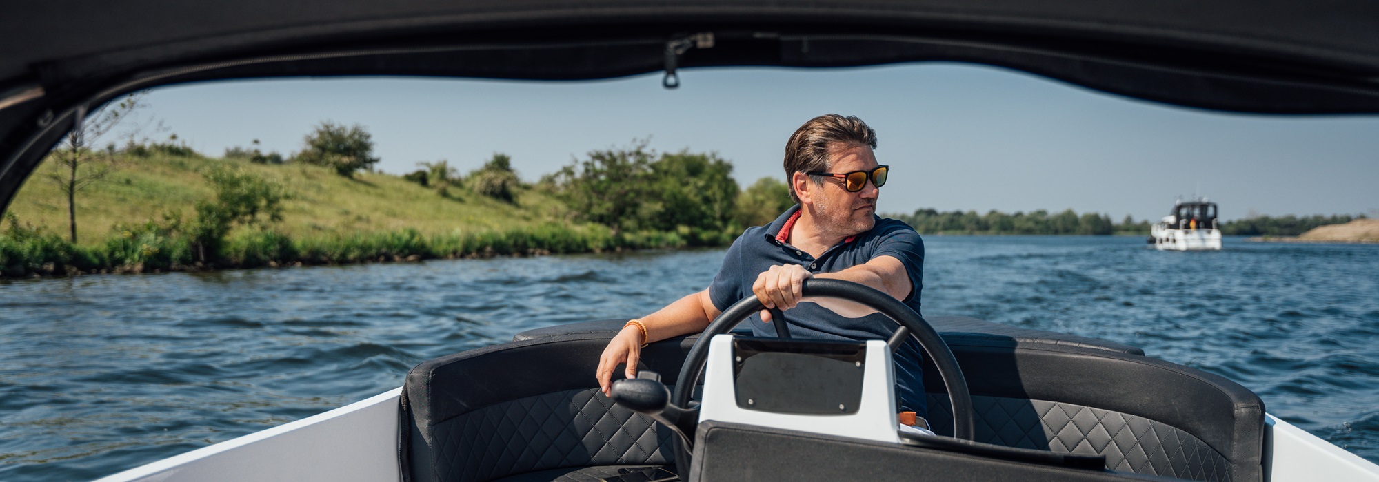 Man stuurt een sloep over de Maasplassen en geniet van een zonnige dag op het water.