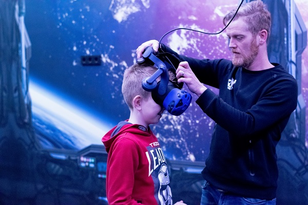 Medewerker van Xbaze in Reuver doet een VR bril op bij een jongen