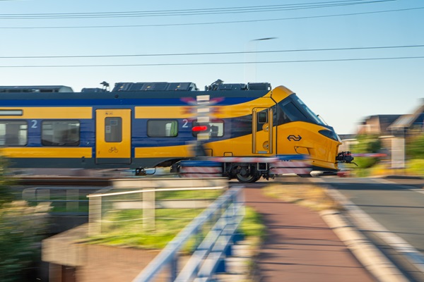 Der neue Zug der NS, der ICNG, rast an einem Bahnübergang, an dem die Lichter rot flackern, voraus