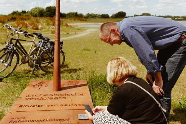 Eine Frau und ein Mann hielten während ihrer Radtour an einem Speer der Archeo Route Limburg an, um mit Hilfe der App zu sehen, was an diesem Ort passiert ist.