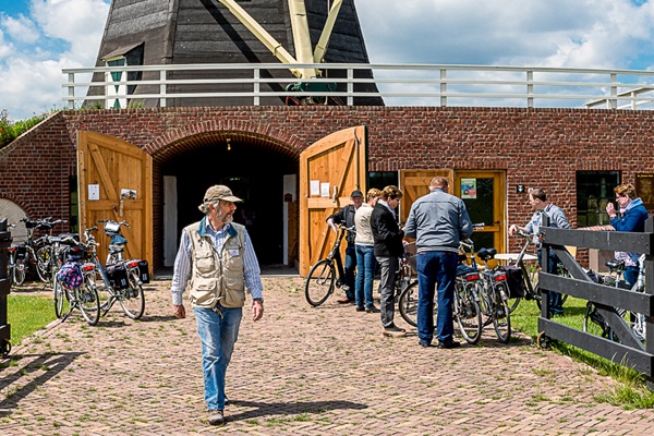 Man loopt weg bij een molen terwijl fietsers afstappen om de molen te bezichtigen