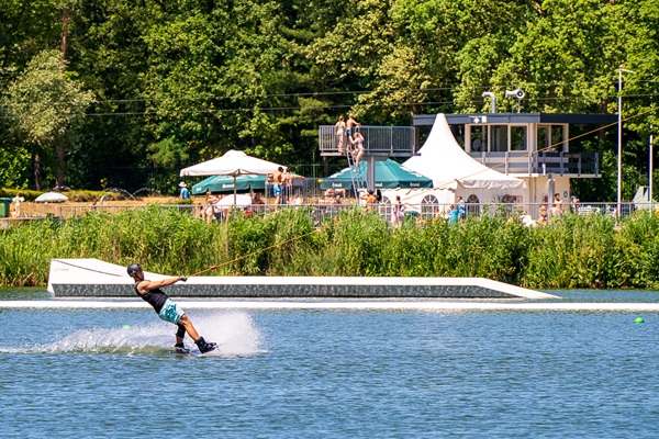 Wakeboarder op snelheid bij recreatiegebied De IJzeren Man in Weert, met toeschouwers op de achtergrond en zomerse sfeer.