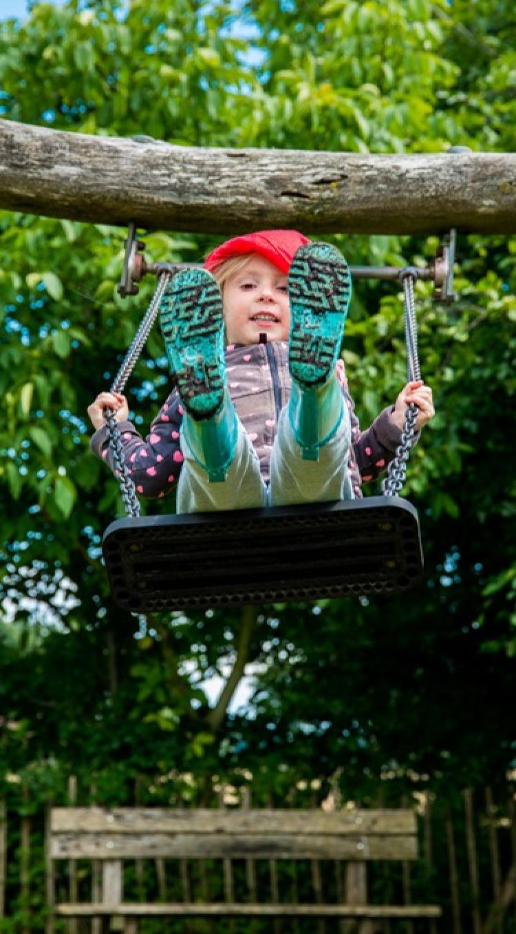 Een meisje met een rode kaboutermuts schommelt in een buitenspeeltuin tijdens een middag vol kinderactiviteiten in het Hart van Limburg.