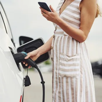 Vrouw kijkt op haar telefoon terwijl ze haar auto aansluit op een elektrisch oplaadpunt in Hart van Limburg