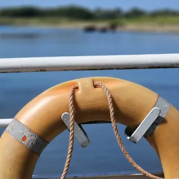 Oranje reddingsboei aan een reling met uitzicht op het water, symbool voor veilig varen.
