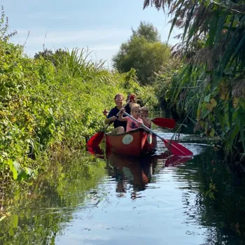 Gezin in een rode kano op de Molenbeek in de gemeente Venray, omgeven door groen en rustig water.