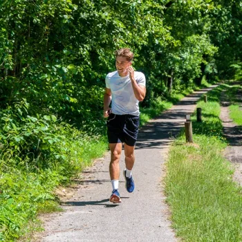 Man jogt op een smal pad door het bos van De IJzeren Man in Weert, op een zonnige dag.