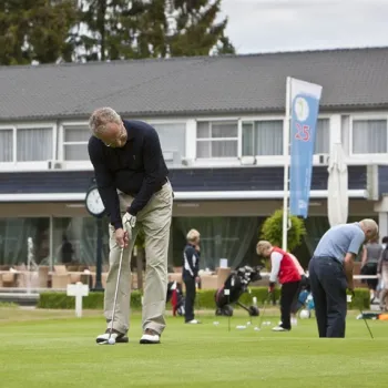 Golfer oefent zijn puttechniek op het terrein van Golfbaan Crossmoor in Limburg, met clubhuis op de achtergrond.