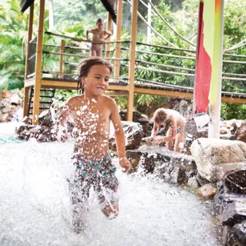 Kind rent lachend door het water in een tropisch binnenzwembad in Limburg tijdens een dag vol kinderactiviteiten.