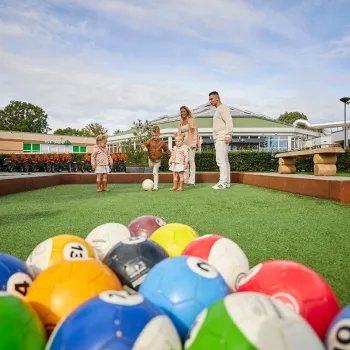 Gezin speelt biljartvoetbal bij de Leistert met grote gekleurde ballen op een kunstgrasveld.